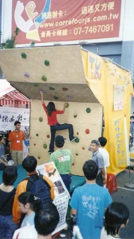 戶外廣場舉辦的小型攀岩體驗活動,一名女子正在攀岩,眾人在旁圍觀