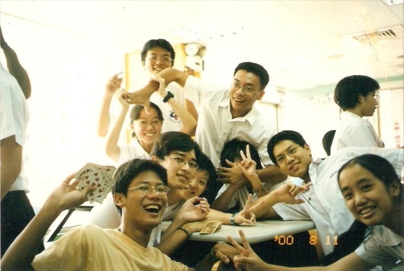 2000年8月一群年輕學生在室內桌前歡樂合影,有人手中拿著撲克牌。