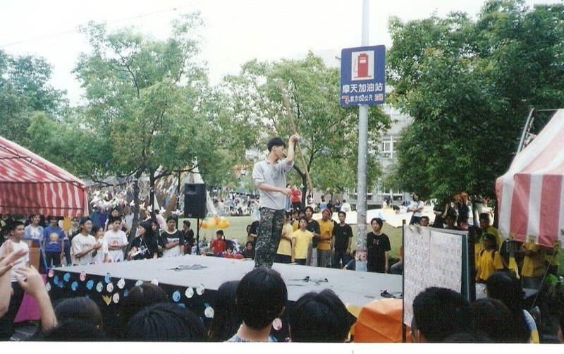 TK在校園戶外舞台上持長棍表演,台下聚集眾多學生觀看